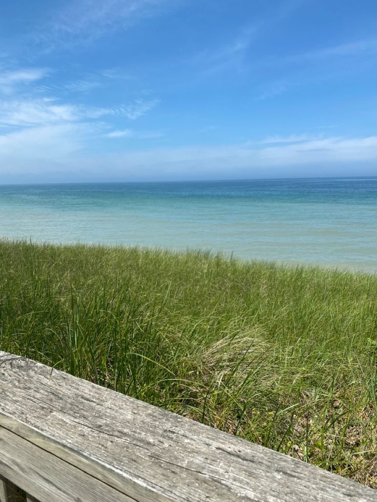 a wooden bench sitting on top of a grass covered field next to the ocean and beach