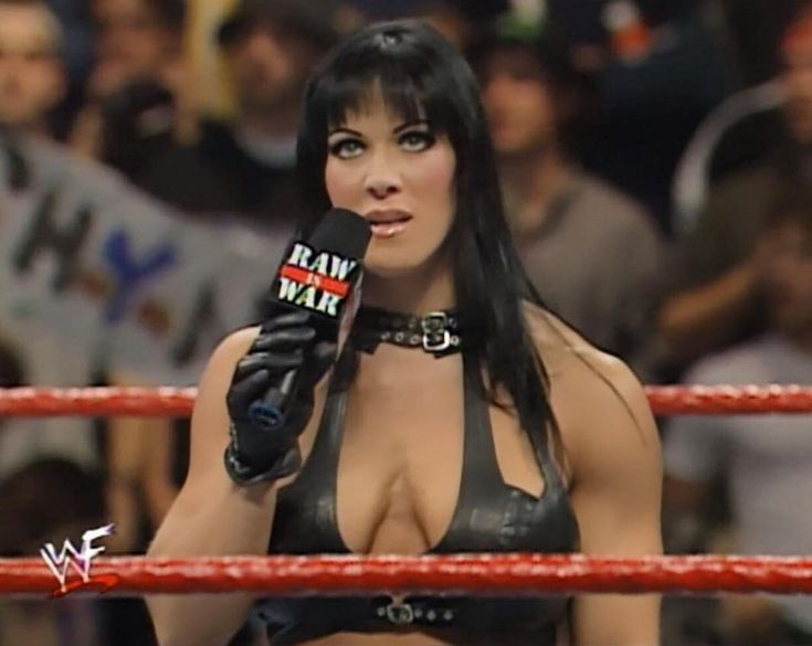 a woman in a leather outfit holding a microphone next to a wrestling ring with people watching