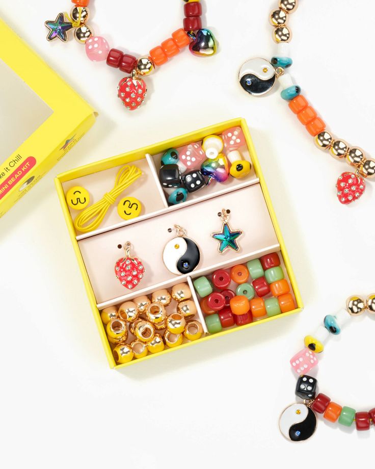 an assortment of beads and bracelets in a yellow box on a white surface next to a card board