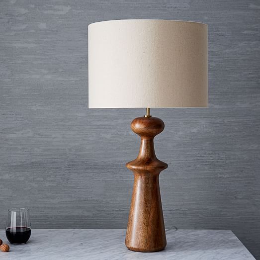 a wooden table lamp with a white shade next to a glass of wine and nuts