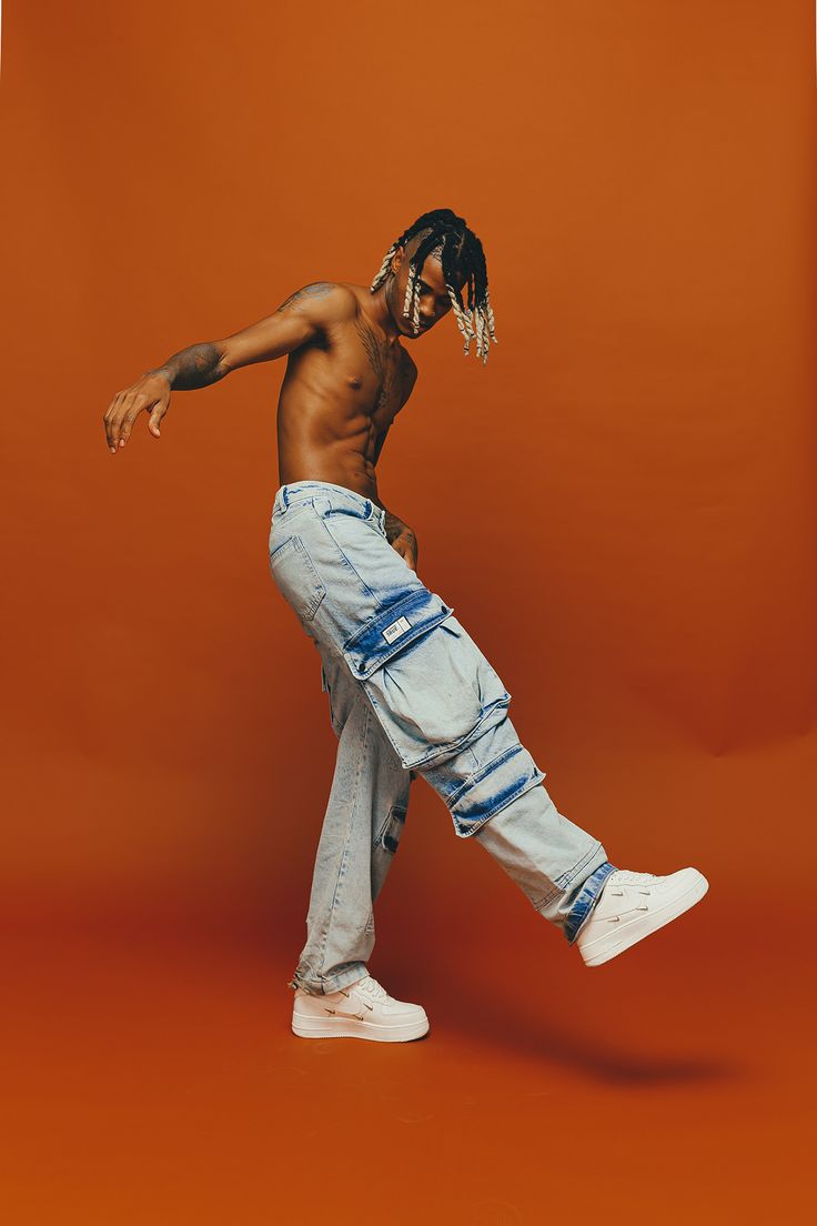 a man with dreadlocks is dancing on an orange background in jeans and sneakers