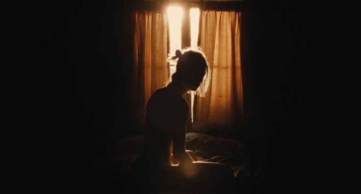 a woman sitting in front of a window with the light shining on her face and head