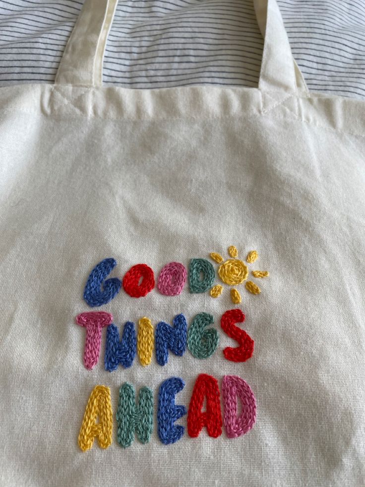 a white bag with the words good things ahead written in multicolored crochet