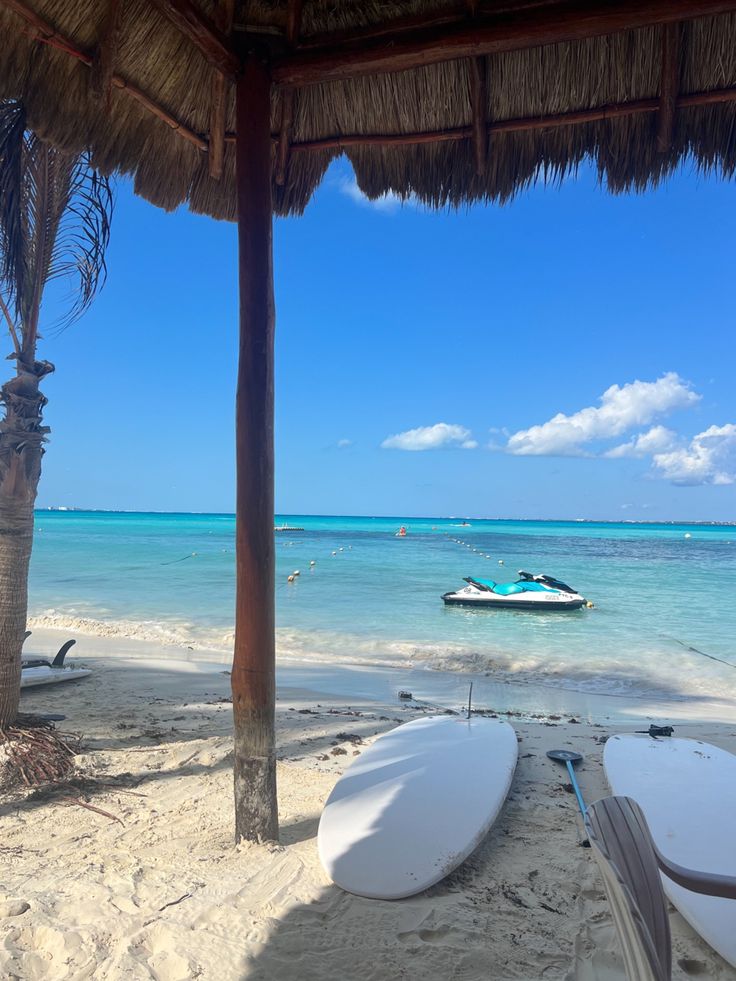 two surfboards sitting on the beach under a thatched roof next to the ocean