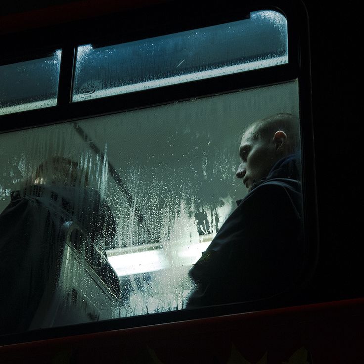 a man sitting on a bus looking out the window at rain falling down from behind him