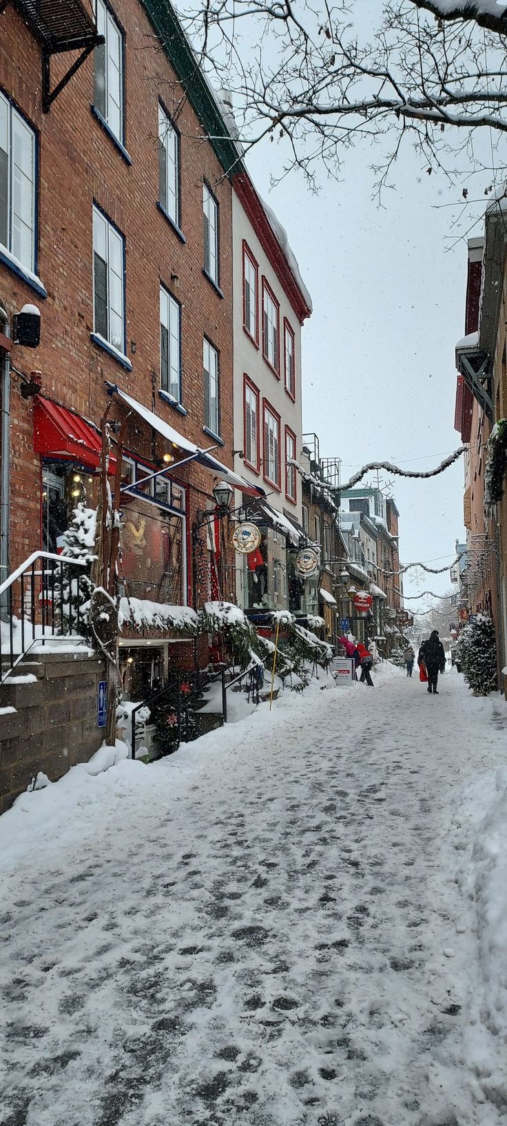 people walking down a snowy street in front of brick buildings and shops with snow on the ground