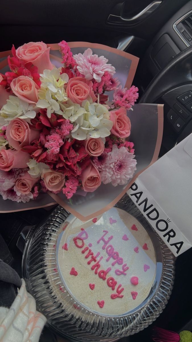 a birthday cake and bouquet of flowers on a table in the back seat of a car