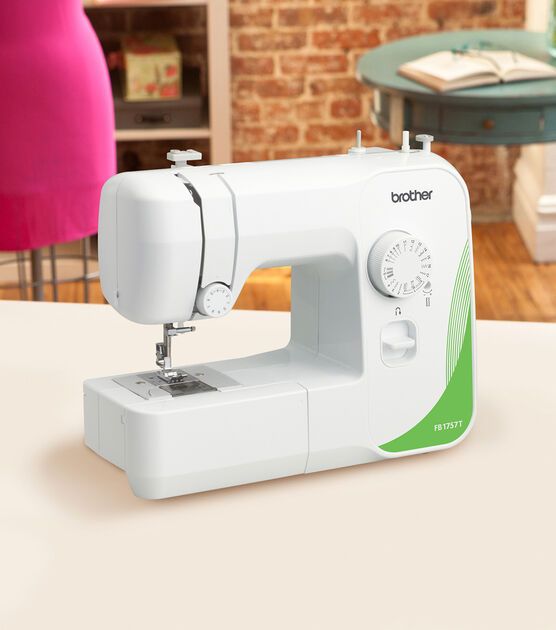 a white sewing machine sitting on top of a table next to a pink chair and brick wall