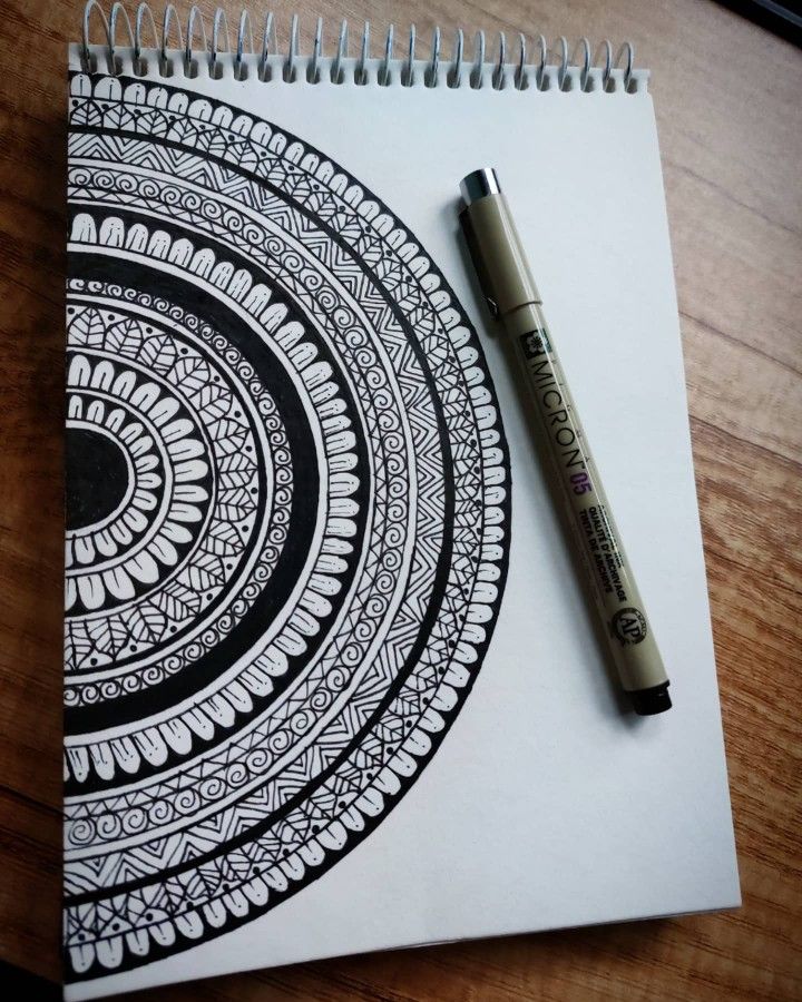 a pen is sitting on top of a spiral notebook with an intricate design in black and white