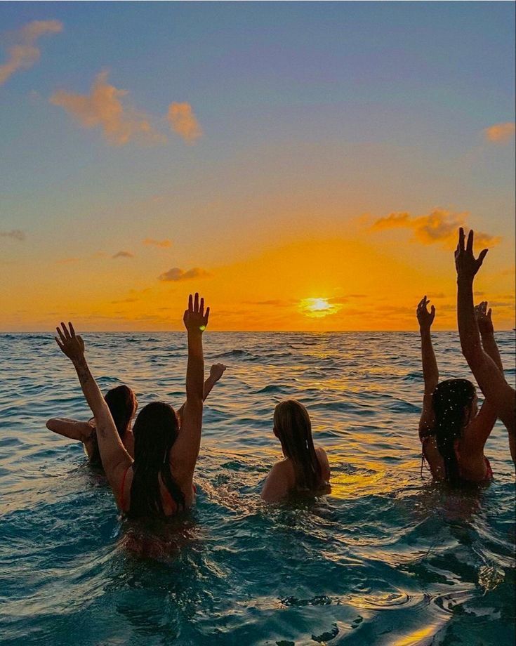 three girls in the water playing with a frisbee while the sun is setting