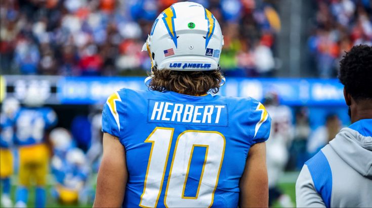 a football player wearing a helmet on the sidelines during a game in front of an audience