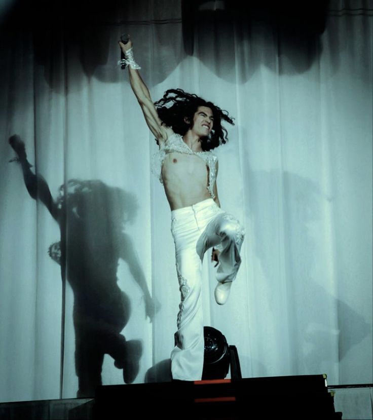 a man with long hair and white pants on stage