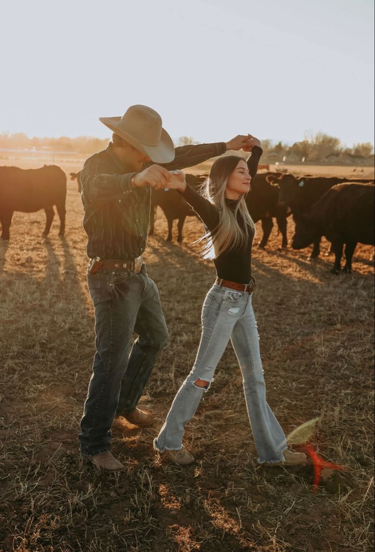 a man and woman are dancing in front of cows on a farm with the sun behind them