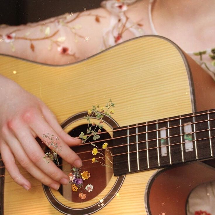 a woman playing an acoustic guitar with flowers on her finger and nails painted on her fingers