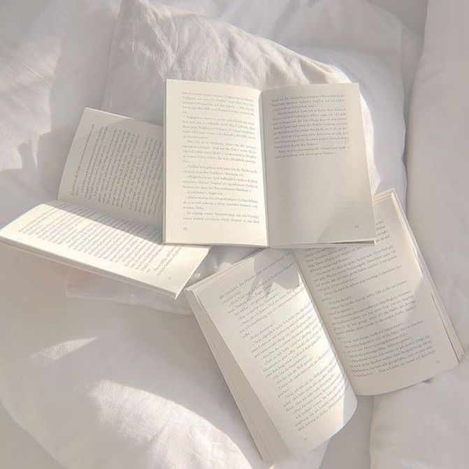 four open books sitting on top of a white bed in front of an unmade pillow