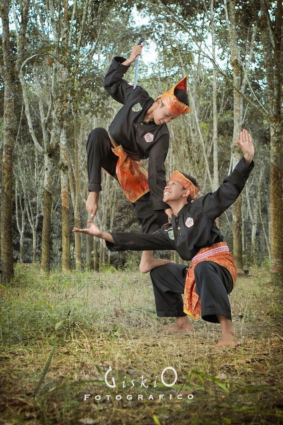 two people in black and orange outfits doing aerial acrobatic tricks with trees in the background