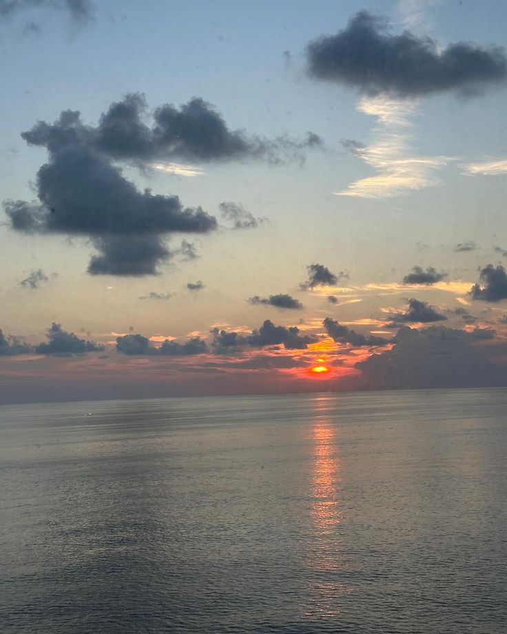 the sun is setting over the ocean with some clouds in the sky and on the water