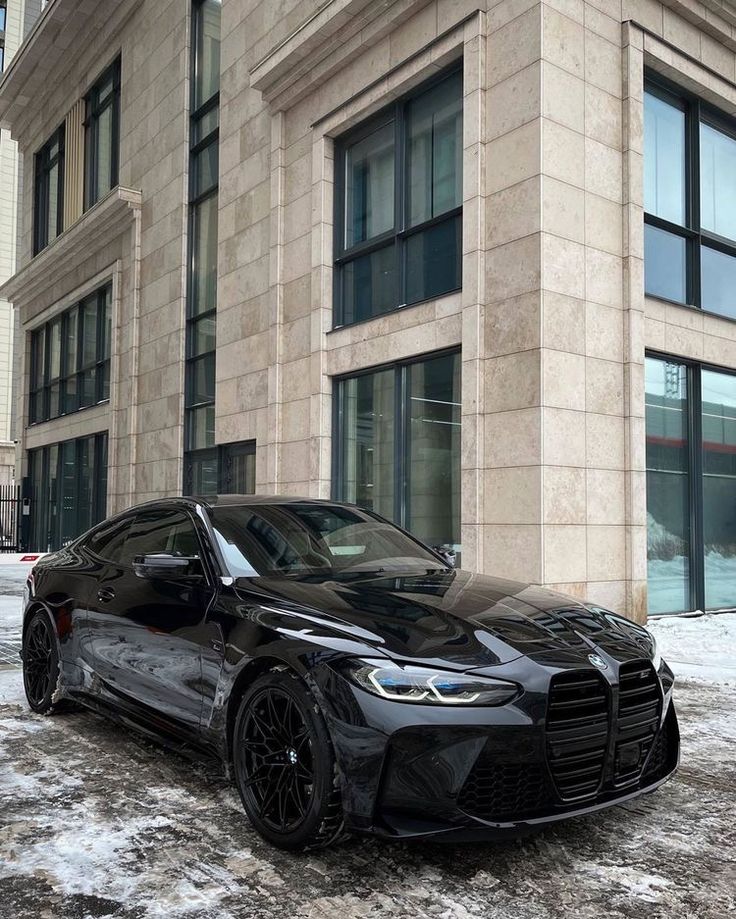 a black sports car parked in front of a large building on a snowy day with no one around