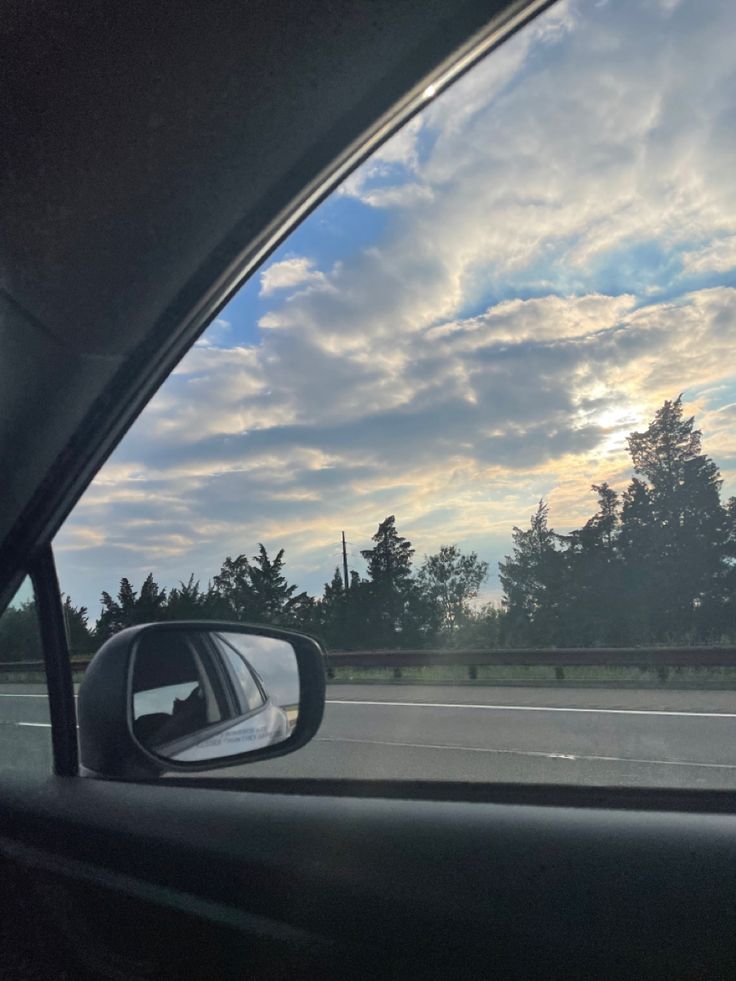 the rear view mirror of a car as it drives down a road with trees in the background