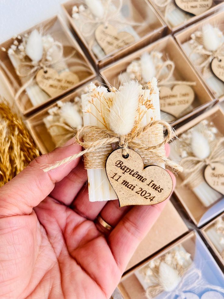 a hand holding a heart shaped candle in front of small boxes with tags on them