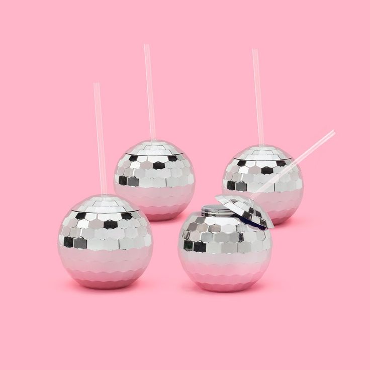 three shiny silver balls with sticks sticking out of them on a pink and white background