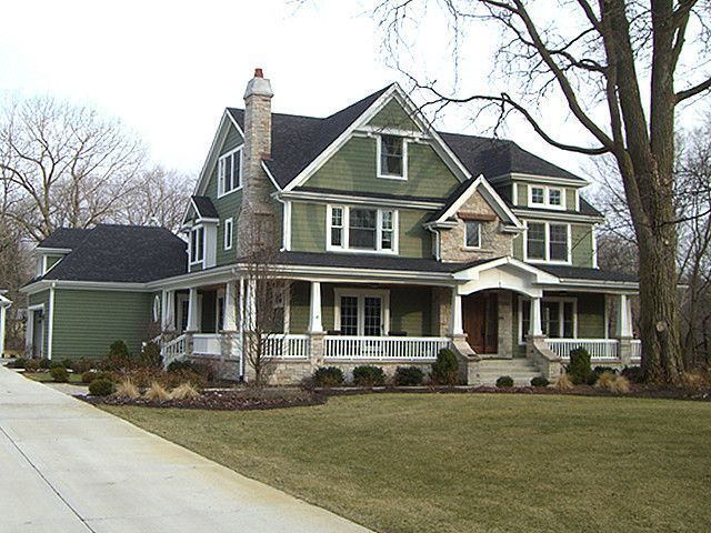 a large green house with white trim on the front porch and two storyed houses