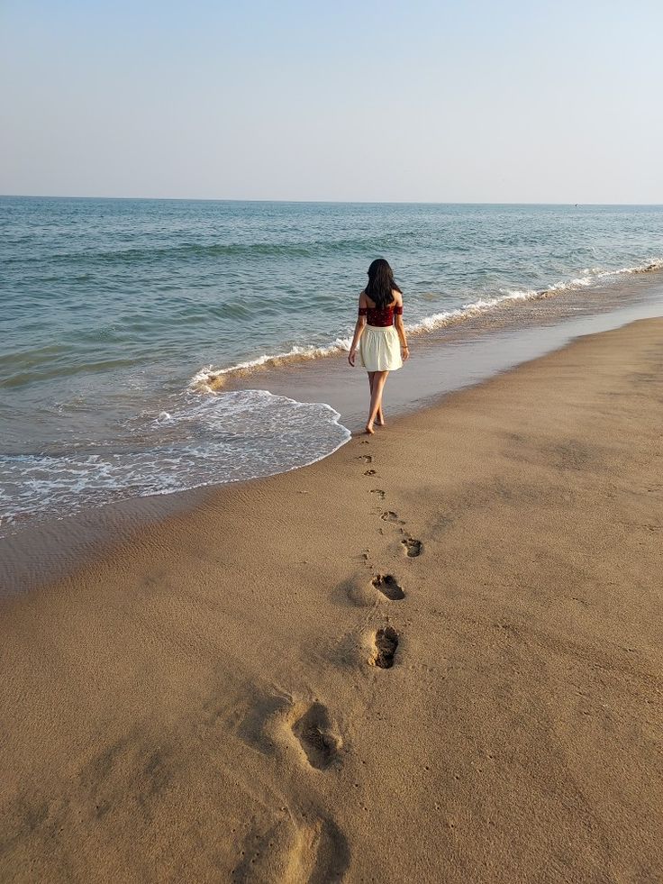 a woman walking along the beach with her footprints in the sand and water behind her