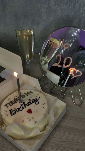 a birthday cake in a box with a lit candle on it and two glasses next to it