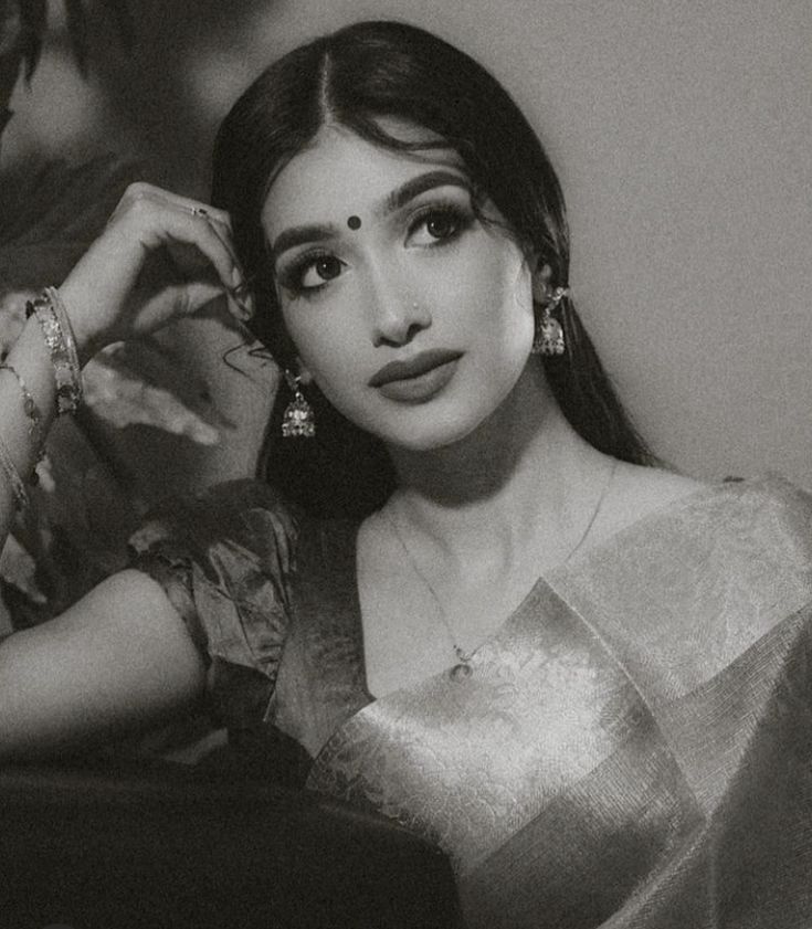 a black and white photo of a woman with long hair in a sari sitting on a couch
