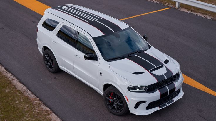 a white dodge van with black stripes driving down the road