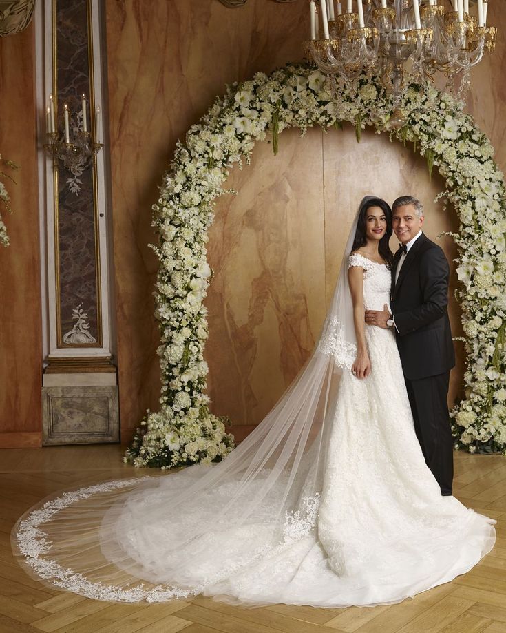 a bride and groom posing in front of a wedding arch with white flowers on it