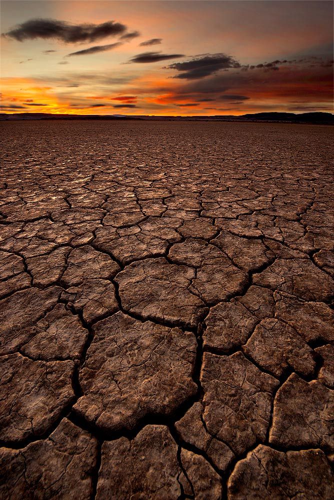 the sun is setting over an arid area with no grass or rocks on it, and there are clouds in the sky