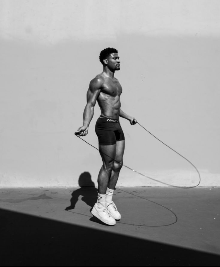 a man with no shirt on holding a rope while standing in front of a wall