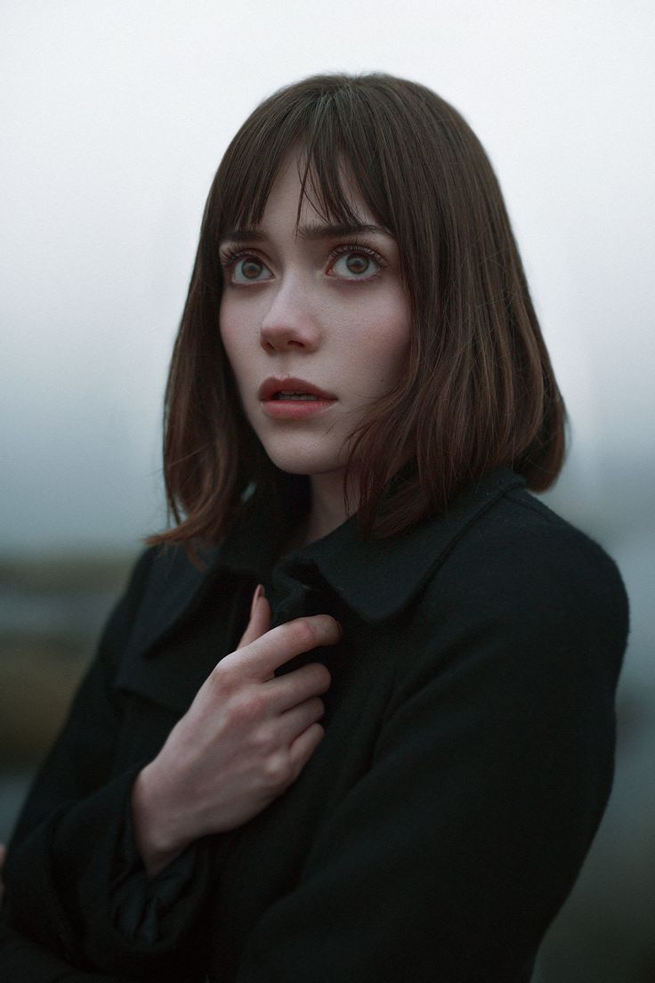 a woman with brown hair and bangs is looking at the camera while wearing a black coat