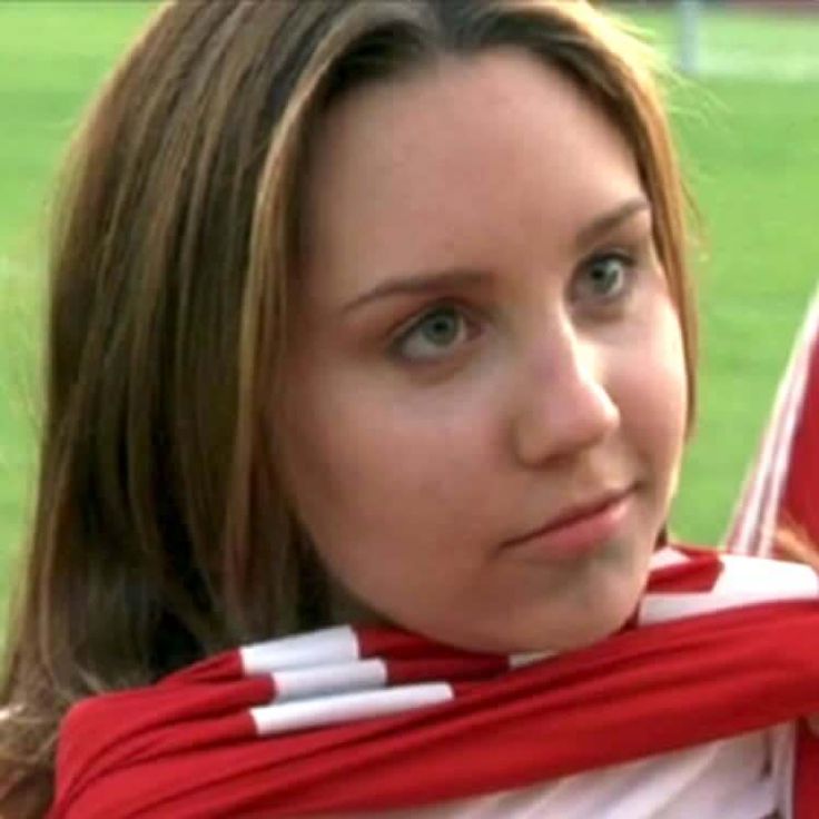 a young woman wearing a red and white scarf on top of her head in front of a soccer field