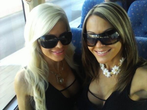 two beautiful young women sitting next to each other on a train together, wearing sunglasses