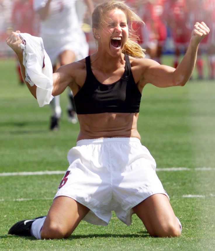 a woman with her arms in the air while sitting on top of a soccer field