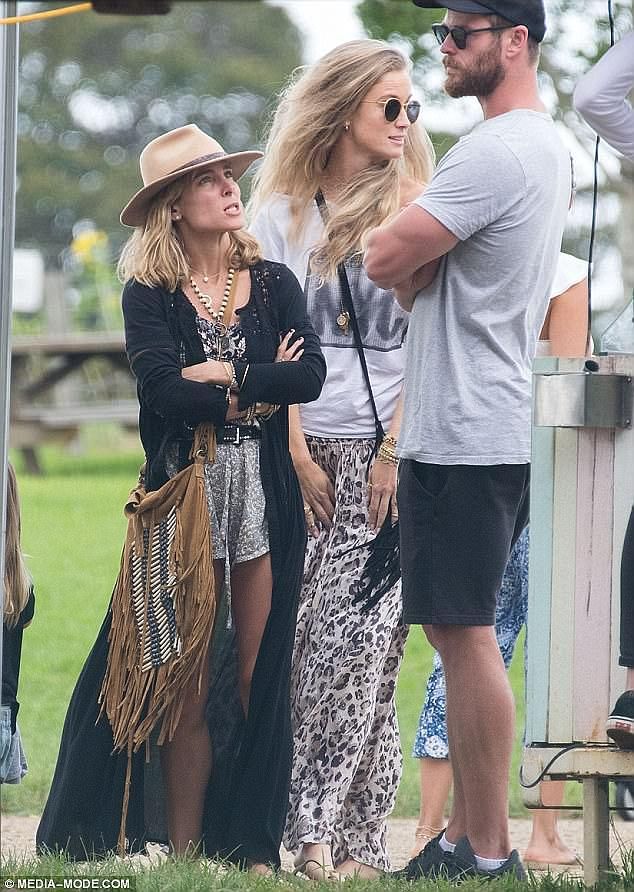 two women and a man are standing under a tent at an outdoor event with other people in the background