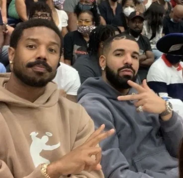 two men sitting next to each other in front of a group of people wearing hoodies