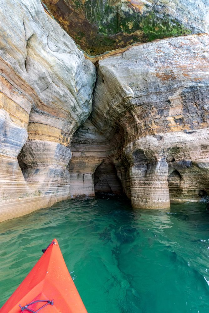 an orange kayak is in the water between two large rock formations, with green waters