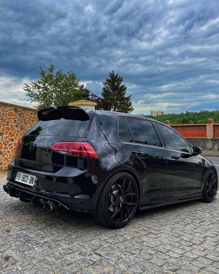 the back end of a black car parked on a cobblestone street with dark clouds in the background