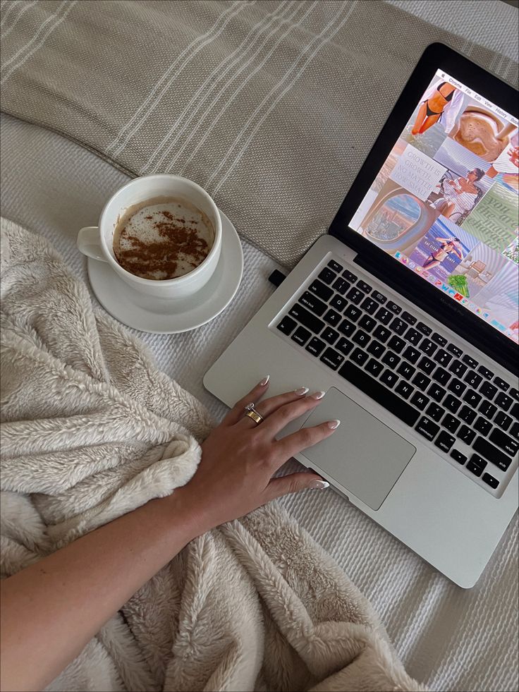 a woman is using her laptop on the bed with a cup of coffee in front of her