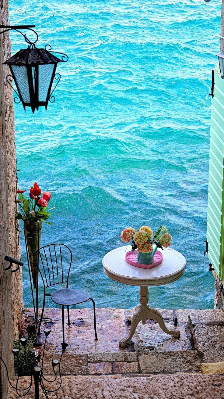 a small table with flowers on it in front of an open door to the water