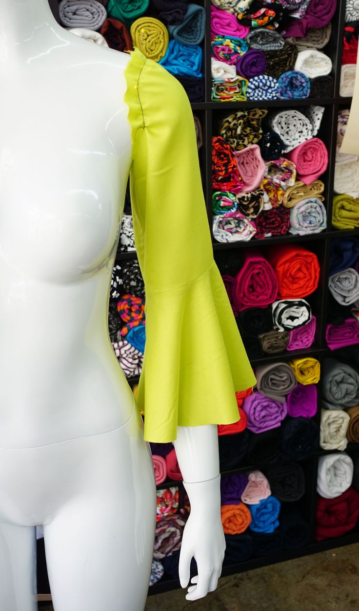 a white mannequin wearing a yellow top in front of a display of colorful scarves