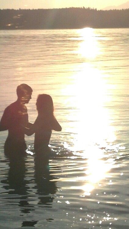 a man and woman standing in the water with their backs to each other as the sun sets