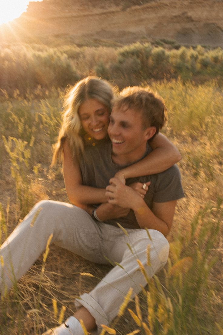 a man and woman sitting on the ground in tall grass with their arms around each other
