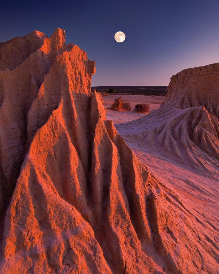 the moon is setting over an eroded area in the desert, with pink hues