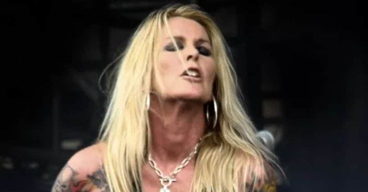 a woman with long blonde hair and piercings on her chest standing in front of a microphone