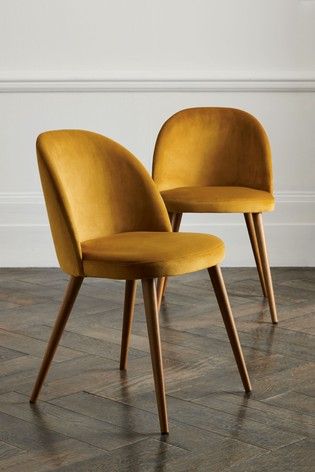 two yellow chairs sitting next to each other on top of a wooden floor in front of a white wall