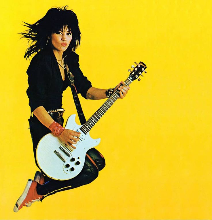 a woman jumping up in the air with a guitar on her feet and holding an electric guitar